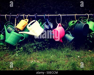 Plastic Watering cans attached to a metal bar on a cemetery in Berlin Kreuzberg Stock Photo