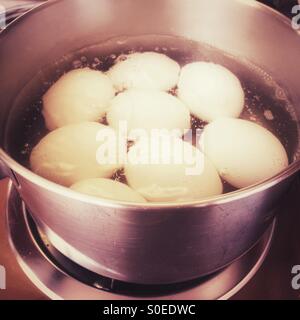 Hard boiled eggs being cooked in a stovetop pan of simmering water. Stock Photo