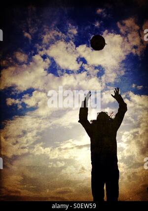 Young girl in silhouette jumping to catch ball Stock Photo