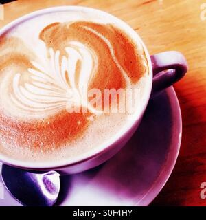 Barista crafted froth design infused over savory organic coffee brewed in a violet cup. Stock Photo