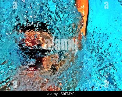 Closeup view above goggled man swimming competition backstroke inundated in wake of water splashes and bubbles. Stock Photo