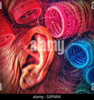 Senior persons ear with coloured hair rollers Stock Photo