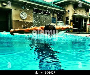 Closeup from the swimmer's lane, this muscular male athlete defies gravity over the water. Butterfly stroke midair closeup view. Stock Photo