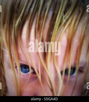 Girl with blue eyes peering out from behind curtain of wet blond hair Stock Photo