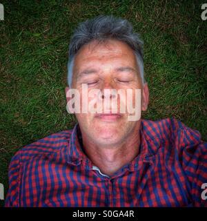 Man with closed eyes lying on grass. Stock Photo