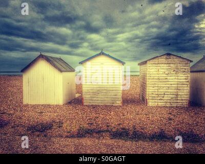 Three painted wooden beach huts on a shingle beach in goring by sea West Sussex UK. Stock Photo