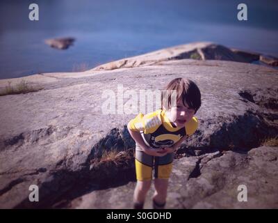 5 year old boy in wetsuit by ocean and rocks. Stock Photo