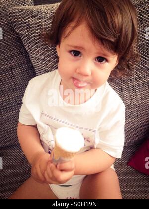 Cute baby girl eating ice cream and sitting on sofa Stock Photo