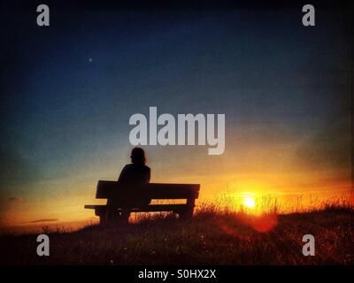 Woman sitting on bench watching the setting sun Stock Photo