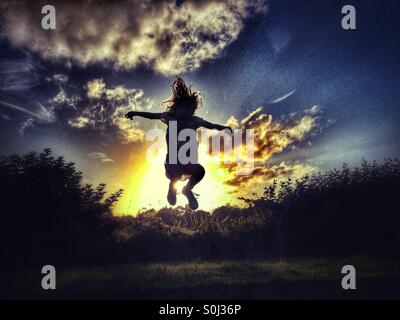 Young girl jumping backlit by late evening sun Stock Photo
