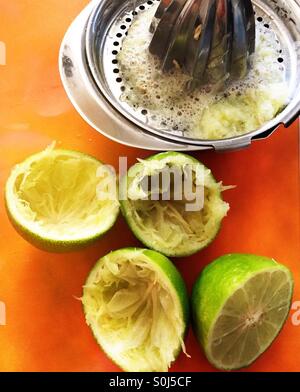 Fresh limes and metal juicer on orange cutting board. Stock Photo