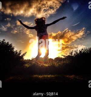 Young girl jumping for joy in silhouette against setting sun Stock Photo
