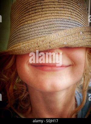 Young girl wearing hat over her eyes and smiling Stock Photo
