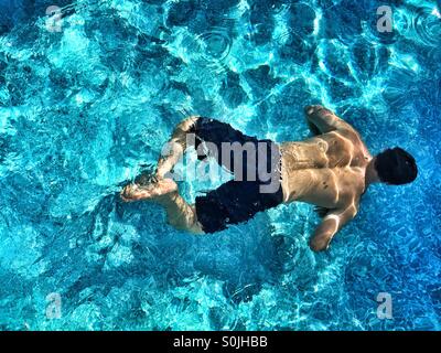 Young man swimming under water in outdoor swimming pool on a sunny day. Photo taken from above. Stock Photo