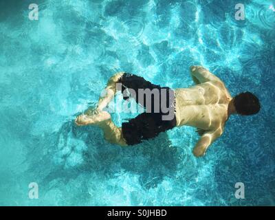 Teenager boy swimming underwater in outdoor swimming pool. Stock Photo