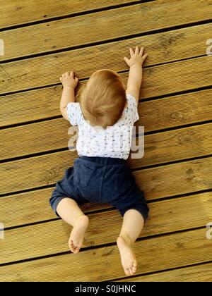 A view from the top of 8 month old baby boy trying to crawl on a wooden deck , outside at the backyard on a warm summer afternoon Stock Photo