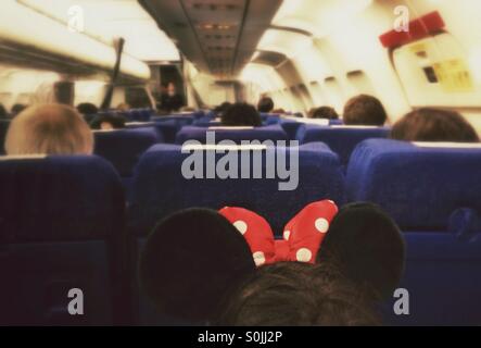 Inside of an airplane with passengers. Girl with Minnie Mouse ears headband in foreground. Stock Photo