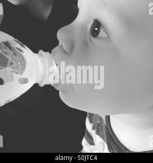 Thirsty baby boy  drinking water out of a bottle, held by his older brother. Stock Photo