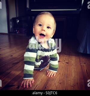 Happy baby boy learning how to crawl on a wooden floor, indoors  in the living room of a Polish  apartment Stock Photo