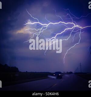 Stormy night. A dazzling bolt of lightning lights up a dusky sky. Light traffic on the road below. Concepts:nature, power, awe. Beyond human. Stock Photo
