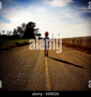 A 7 year old boy stands in the middle of a country road wearing his bicycle helmet. Stock Photo