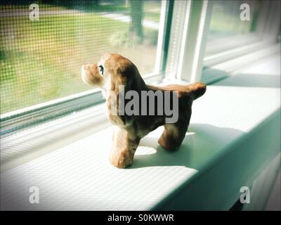 A dog figurine, looking out a window. Stock Photo