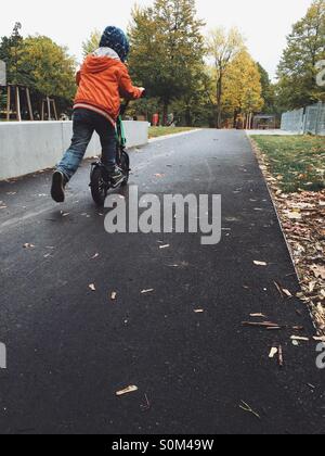 Boy riding a scooter in a park in rainy autumn weather Stock Photo