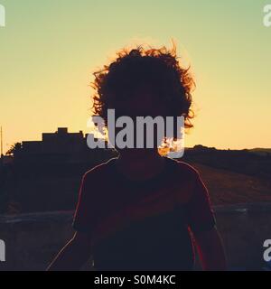 Glowing silhouette of boy with sun going down in background Stock Photo