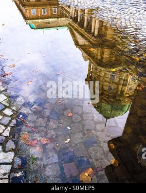 Autumn in Budapest. Buda castle reflecting in a rain puddle on cobblestone pavement. Stock Photo