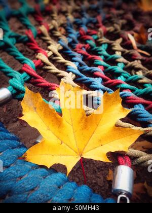 A yellow maple leaf fallen on a children's swing in autumn Stock Photo