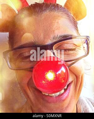 Portrait of a woman laughing and having fun with a blinking red nose and toy reindeer antlers on her head. Stock Photo