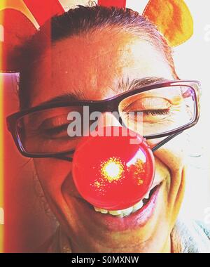 Portrait of a woman laughing and having fun with a blinking red nose and toy reindeer antlers on her head. Stock Photo