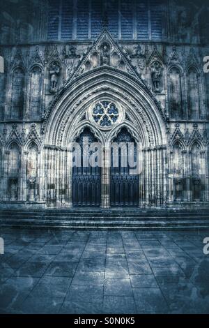 The darkened doors of an English Cathedral. Ornate stonework surrounding thick wooden doors at York Minster. Stock Photo