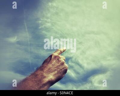 Man's hand with pointing finger appears to draw the clouds in the sky. Stock Photo