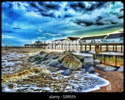 An HDR view of Southwold Pier in January. Small waves the colour of dirty brown water, break over a group of rocks on the Beach. Photo Credit - © COLIN HOSKINS. Stock Photo