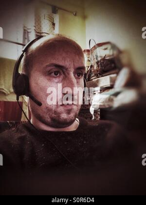 A man sitting down and wearing a computer headset with built in headphones and microphone. Stock Photo