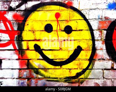 Smiley graffiti with a red dot on the forehead, like a gunshot wound Stock Photo