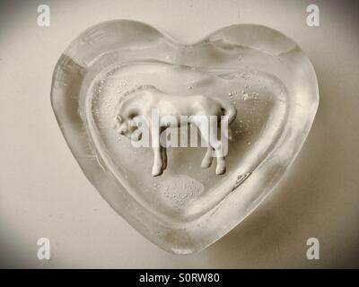 A white horse figurine in an ice block shaped like a heart. Stock Photo