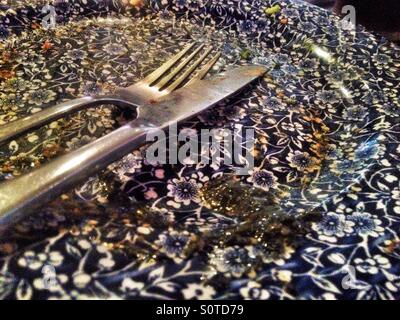 A knife and fork and some mint sauce on an otherwise empty plate at the end of a meal. Stock Photo