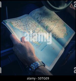 Man with map book of South Africa on lap in car. Stock Photo