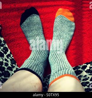 Man wearing  mismatched gray socks with blue and orange toes on a leopard and red squared rug Stock Photo