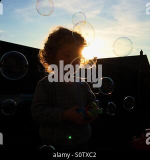 Silhouetted child playing with bubbles in garden Stock Photo