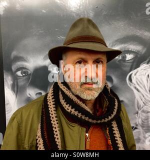 Bearded man in scarf and hat being watched by eyes behind him Stock Photo