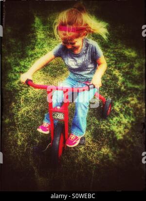 Girl riding a vintage Locomotion tricycle in the grass Stock Photo