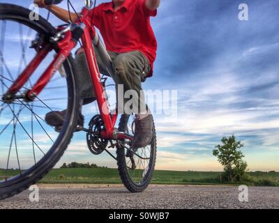 View looking up at a boy riding past on his red bicycle Stock Photo