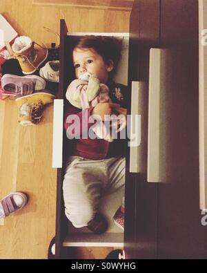 Cute little girl lying in shoe closet shelf top view Stock Photo