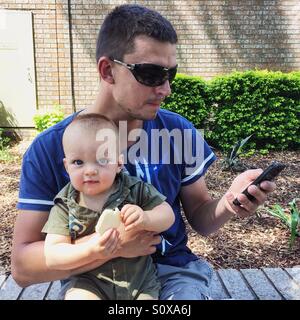 Father holding baby and looking at mobile phone Stock Photo