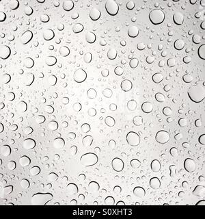Raindrops on a clear glass pane, macro photography showing water droplets and light refractions on a window during rainfall. Stock Photo