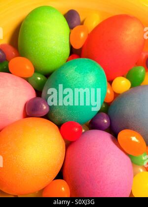 Brightly colored eggs and jelly beans in a yellow bowl, close-up view Stock Photo