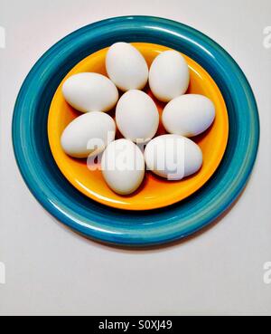 Whole white eggs in yellow and blue bowl overhead view on white background Stock Photo